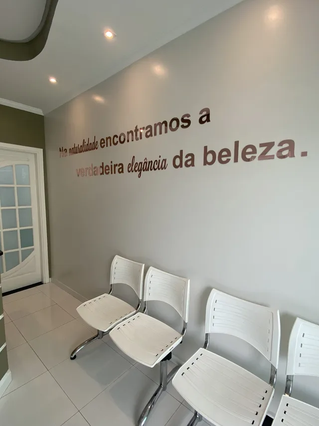 Sala de espera com cadeiras brancas e a frase na parede: na simplicidade encontramos a verdadeira elegância da beleza